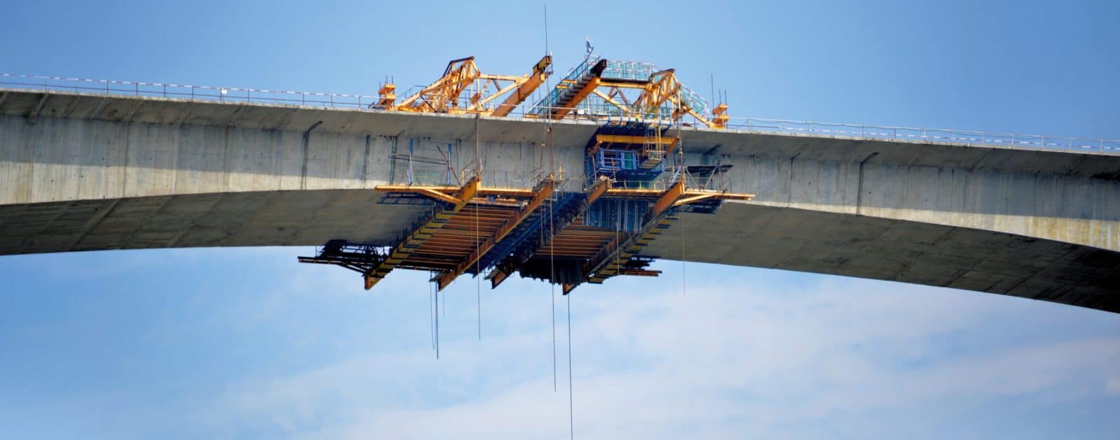 Kran und Baugerüst beim Bau einer Brücke gegen blauen Himmel.