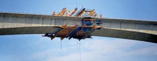 Kran und Baugerüst beim Bau einer Brücke gegen blauen Himmel.