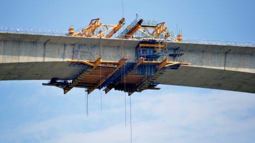 Kran und Baugerüst beim Bau einer Brücke gegen blauen Himmel.