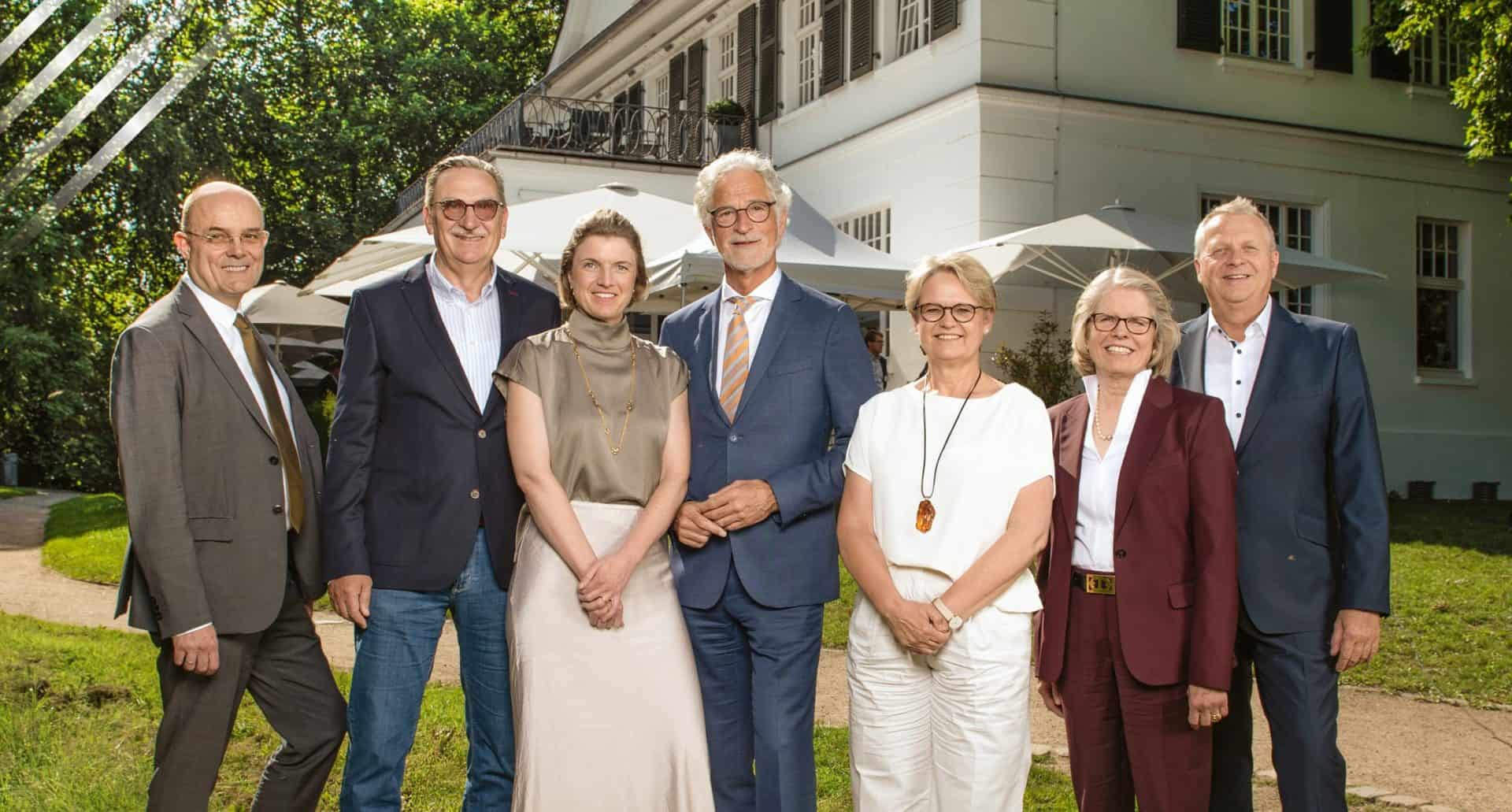 Gruppenfoto im Garten mit sieben Personen bei sonnigem Wetter.
