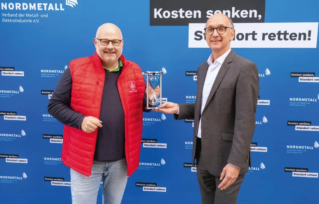 Zeit ist Geld: Dr. Peter Schlaffke (r.), stellvertretender NORDMETALL-Hauptgeschäftsführer, überreicht dem Bezirksleiter der IG Metall Küste, Daniel Friedrich, eine Sanduhr aus Metall.